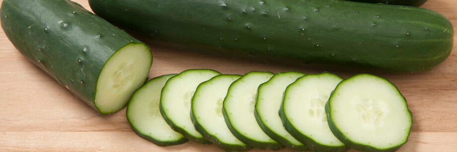 The fruit of one of our slicing cucumber varieties is laid out, whole and sliced, on a wood cutting board.